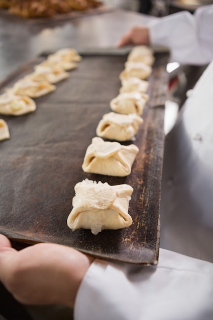 Close up of baker holding tray of raw dough