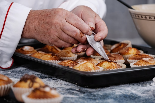 Close-up of baker's hands putting chocolate on muffins