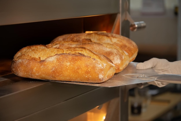 Close-up di una pala di panettiere che tira fuori il pane artigianale appena cotto dalla produzione di pane in forno