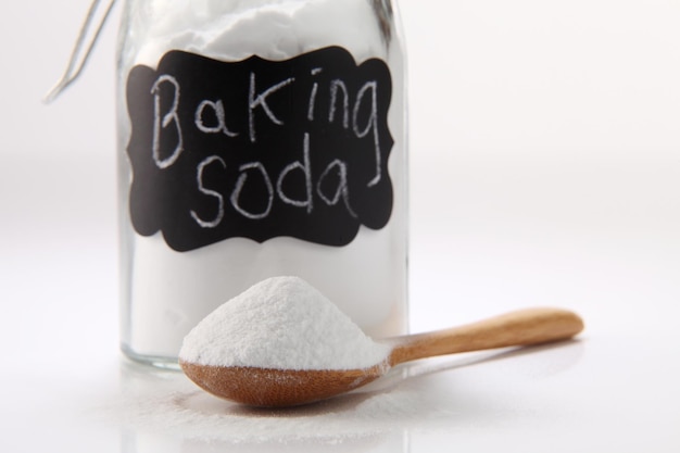 Close-up of baking soda in jar and wooden spoon against white background