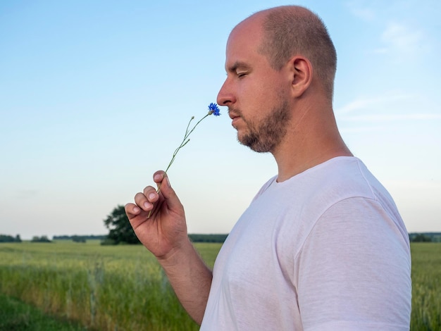 Close-up of a bald man with his eyes closed sniffing a flower.