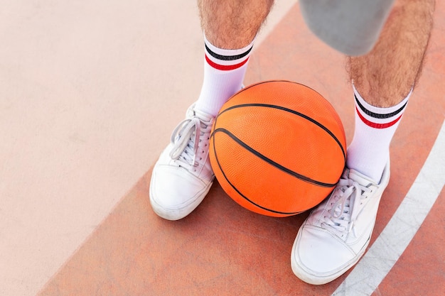 Foto primo piano di una palla trattenuta tra i piedi di un uomo su un campo da basket concetto di sport urbano in strada copia spazio per il testo