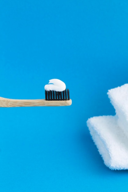 Close-up on bamboo toothbrush with white paste and white  towels on the blue background. Location vertical.