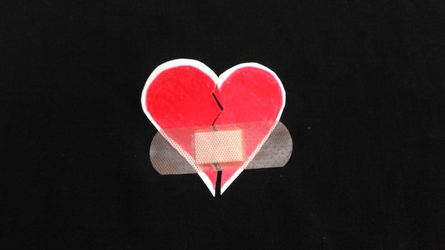 Photo close-up of bandage on broken heart shape over black background