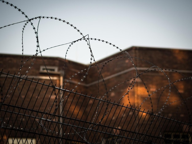 Photo close-up of barbed wire fence against brick building and sky