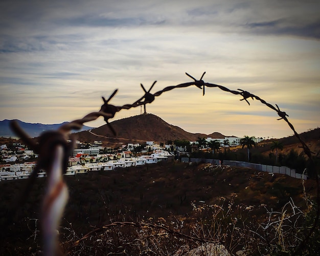 Photo close-up of barbed wire with city in background against sky
