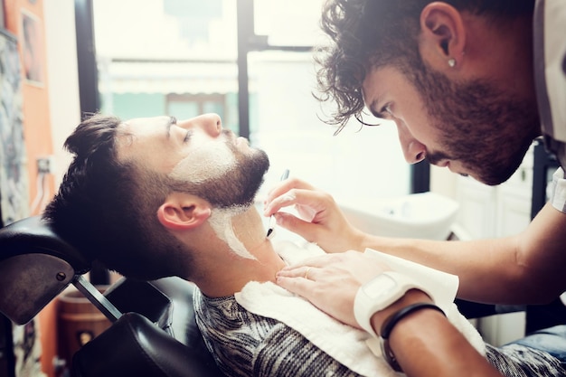 Close-up of barber shaving customer beard at salon