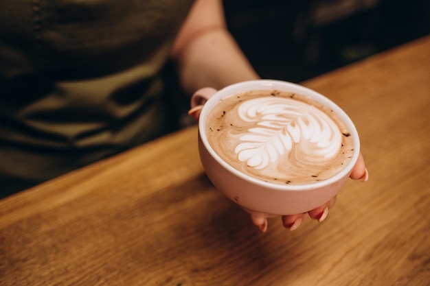 ラテ アートを作るためのコーヒー カップに温かいミルクを注ぐバリスタの手を閉じる