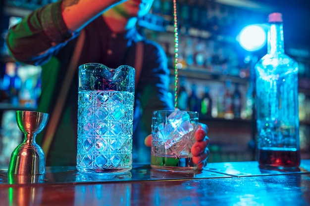 Close up of barman finishes preparation of alcoholic cocktail in multicolored neon light