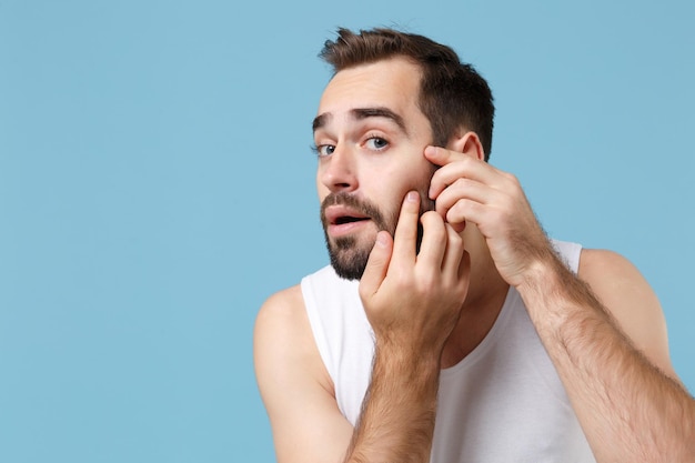 Close up bearded young man 20s years old playing with his face\
in white shirt isolated on blue pastel background, studio portrait.\
skin care healthcare cosmetic procedures concept. mock up copy\
space.