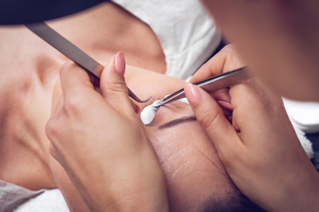 Close-up of a beautician hands applying extended eyelashes to model.