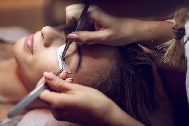 Close-up of a beautician hands applying extended eyelashes to model.