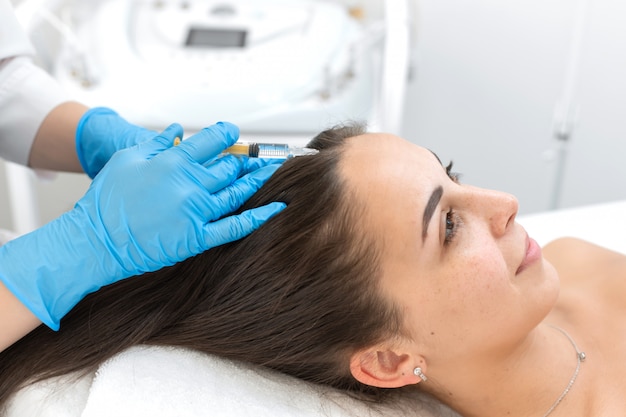 Close-up, the beautician makes injections of vitamins into the scalp for strengthening the hair