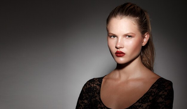 Photo close up of a beautiful blonde girl with hair gathered in a ponytail with red lips on dark background. copy space.