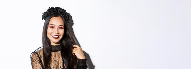 Photo close-up of beautiful elegant asian woman in black wreath and gothic lace dress smiling standing over white background dressed-up for halloween party             person