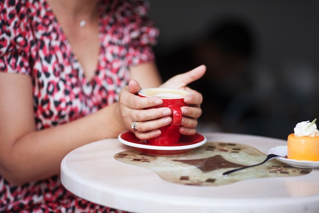 クローズアップの美しい女性の手は、温かい飲み物で赤いカップを抱きしめます。カフェで一杯のコーヒーを保持している女性の手