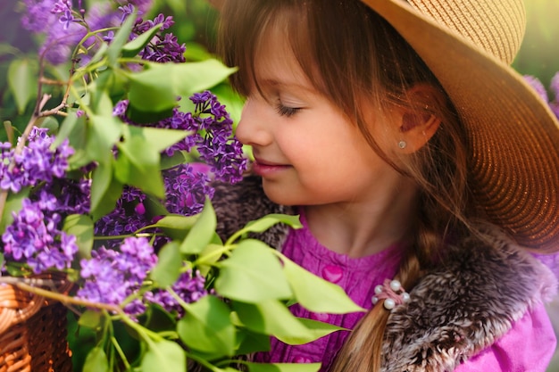 Close up beautiful girl in straw hat in lilac Garden Girl with lilac flowers in springtime Gardening