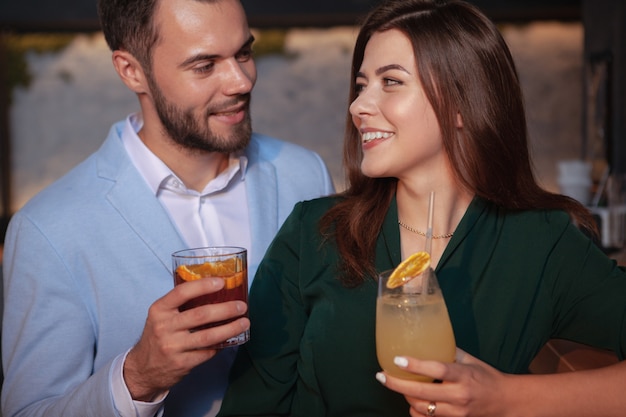 close up of a beautiful loving couple smiling at each other, enjoying drinks at cocktail bar