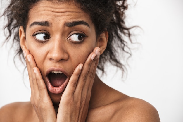 Close up of a beautiful shocked young topless african woman posing over white