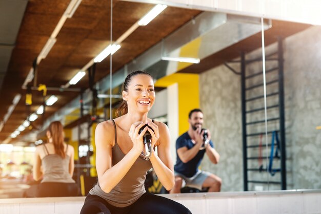 포니 테일 kettlebell와 함께 운동을 하 고 아름 다운 웃는 백인 여자의 닫습니다. 배경 거울과 반사에 남자.