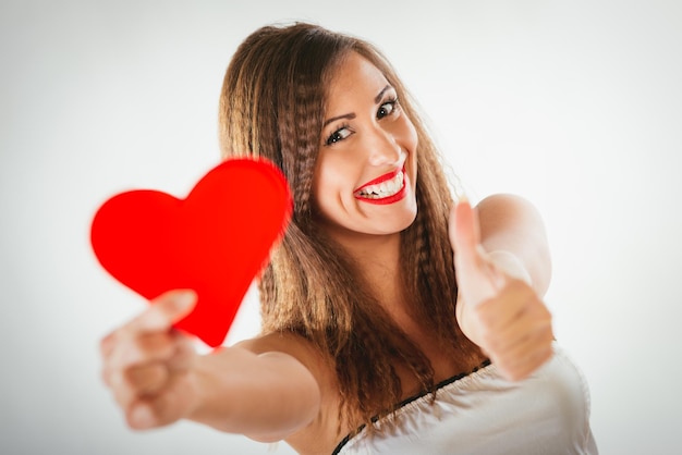 Foto primo piano di bella ragazza sorridente che tiene un cuore rosso con il tumb up. messa a fuoco selettiva. concentrati sulla ragazza.