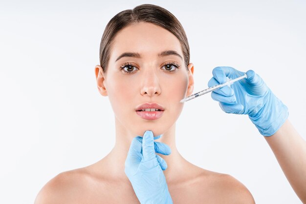 Close up of beautiful woman gets injection in her lips isolated over white background