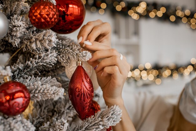 Close up of beautiful woman hands decorating New Year tree with Christmas lights as a background