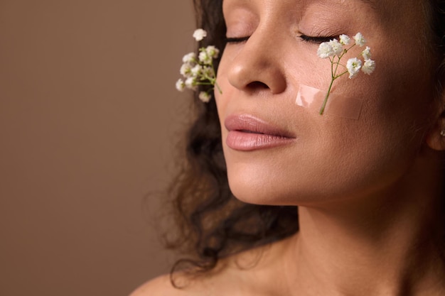 Close-up beautiful woman's face with Gypsophila white sprig on cheeks. Spring, femininity, sensuality, natural beauty people and Women's Day concept on beige background with copy ad space