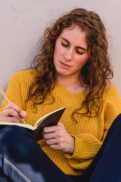 Close up of beautiful woman sitting at the street outdoors, taking notes in a notebook