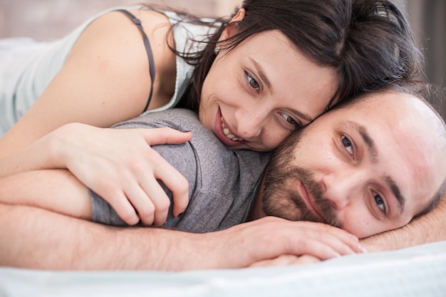 Close up of beautiful woman smiling after waking up in the morning and laying on her boyfriend back.