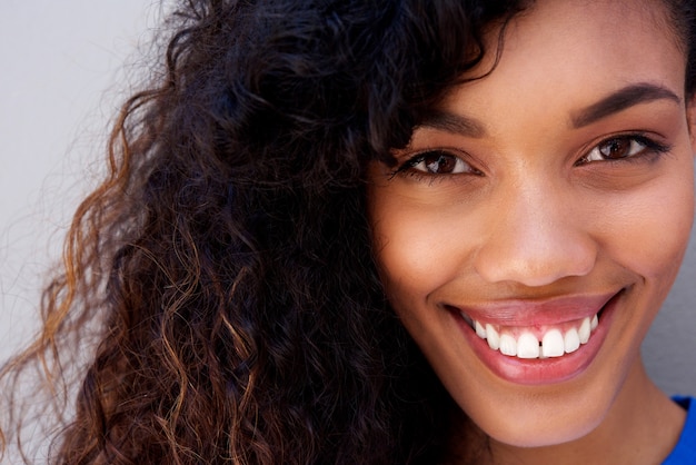 Close up beautiful young african american woman with curly hair smiling against gray backgorund