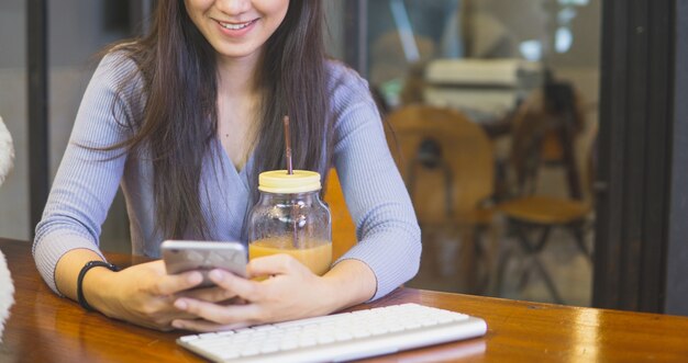 カフェで美しい若いアジアの女性を閉じて、携帯電話とコーヒーを飲む