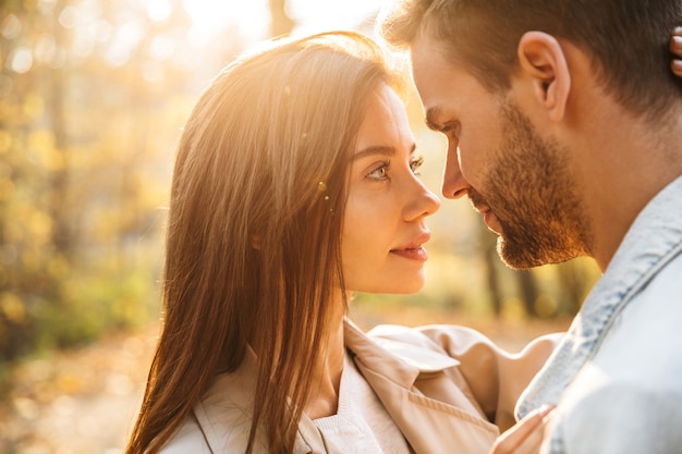 Close up of a beautiful young happy couple in love embracing while spending time in the autumn park