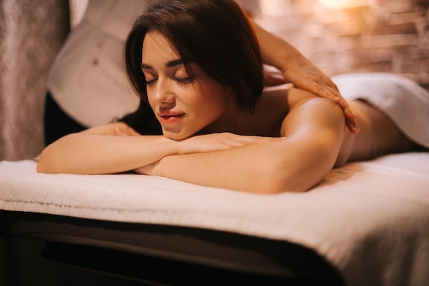 Primo piano di bella giovane donna con massaggio alla schiena nel salone spa sdraiato sul lettino da massaggio, distogliendo lo sguardo. concetto di massaggio professionale di lusso. concetto di cura del corpo.