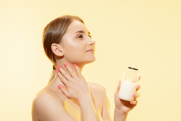 Close up of beautiful young woman massaging skin with moisturizer yellow