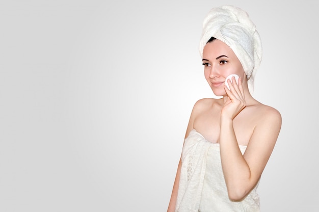ローションに浸したシャワーワイプの顔のコットンパッドの後、頭の上に白いタオルで美しい若い女性を閉じます。スパのコンセプト