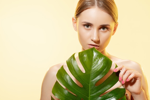 Close up of beautiful young woman with green leaves on white background.