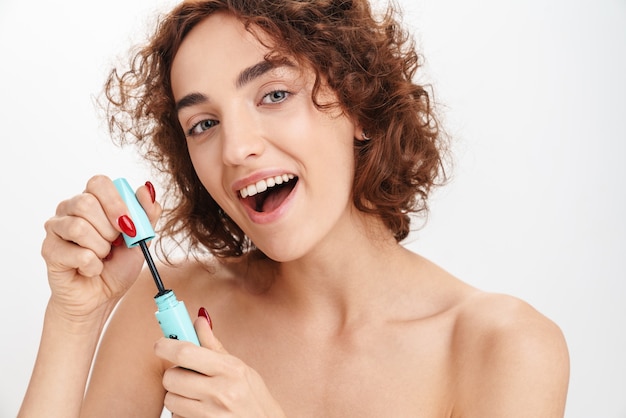 Close up beauty portrait of an attractive smiling young topless woman with short curly brown hair isolated over white wall, showing mascara