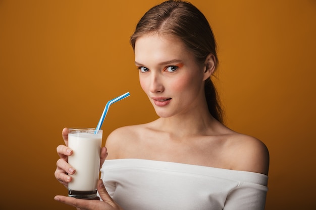 Close up beauty portrait of a beautiful sensual young woman isolated over beige background, holding glass of milk with a straw