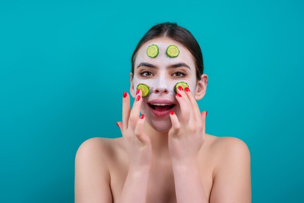 Close up beauty portrait of a beautiful woman applying face cream and facial mask of cucumber mask f