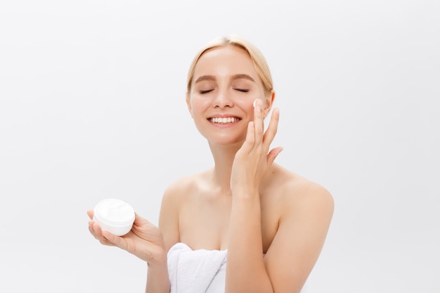 Close up beauty portrait of a laughing beautiful half naked woman applying face cream 