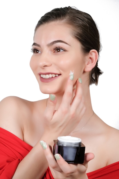 Close up beauty portrait of a laughing beautiful woman applying face cream and staring isolated