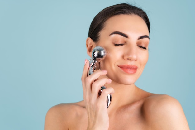 Close up beauty portrait of a woman with perfect skin and natural make-up, plump nude lips, holding a roller massager for face and neck