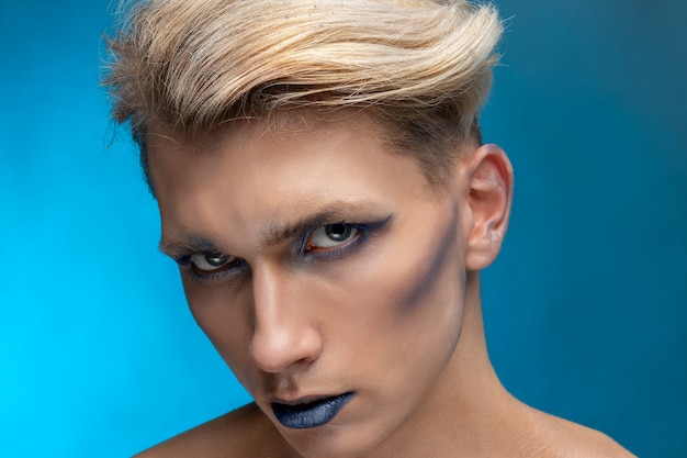Close-up beauty portrait of a young man with professional makeup and blond flying hair