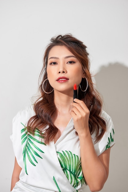 Close up beauty portrait of young woman with clean fresh perfect skin and nude makeup look at camera and holding lipstick