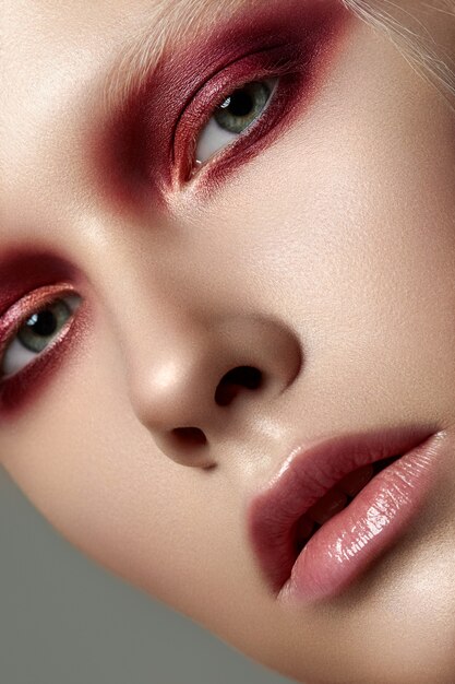 Close up beauty portrait of young woman with white brows and red smokey eyes. Perfect skin and fashion makeup. Sensuality, passion, trendy youth makeup concept.