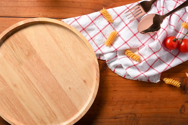 Close-up beeld Lege houten plaat zilverwerk rauwe pasta verse tomaten tafelkleed op houten tafel