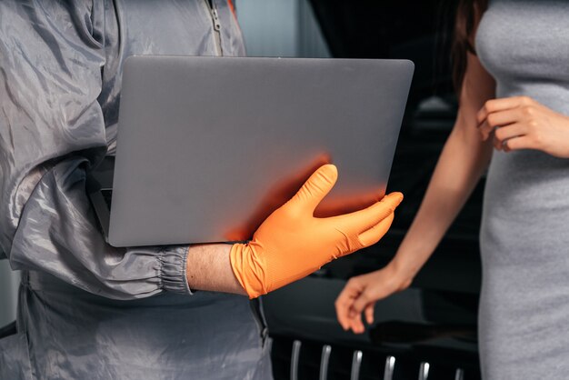 Close-up beeld van automonteur die communiceert met een vrouwelijke klant terwijl hij een laptop gebruikt en onderzoekt