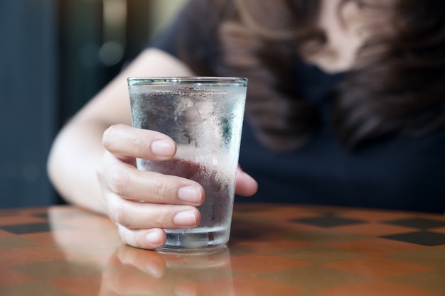 Close-up beeld van de hand van de vrouw met een glas koud water op tafel