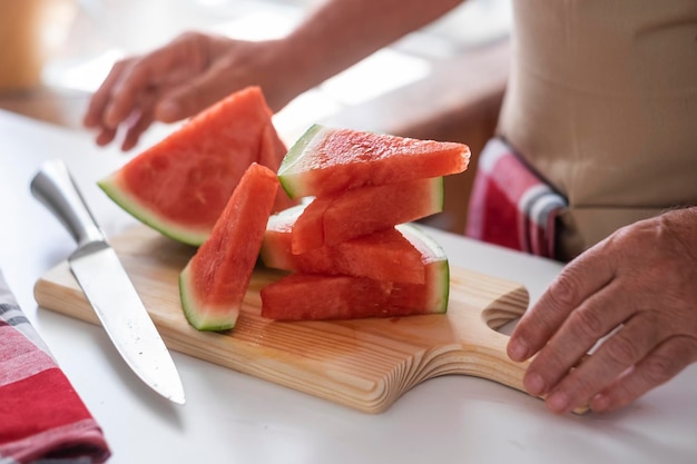 Close-up beeld van de handen van een bejaarde en een houten snijplank met plakjes vers gesneden watermeloen gezond en vegetarisch eten